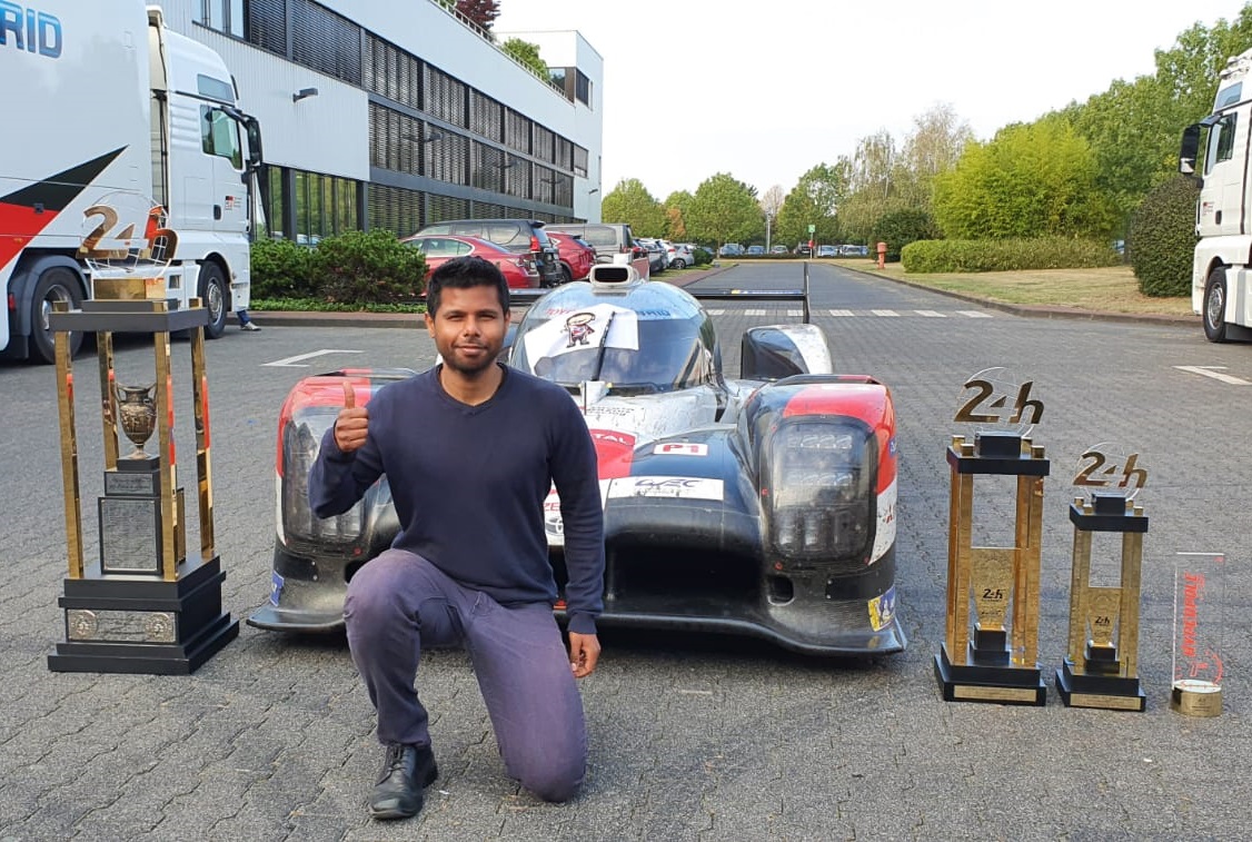 A photo of Hemanth posing in front of the Le Mans 24 hours championship winning car including the various category trophies.