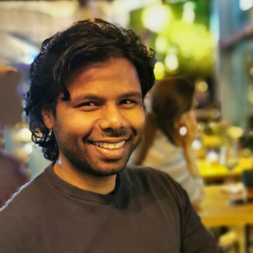 A photo of Hemanth smiling with a buzzling oriental restaurant in the background.